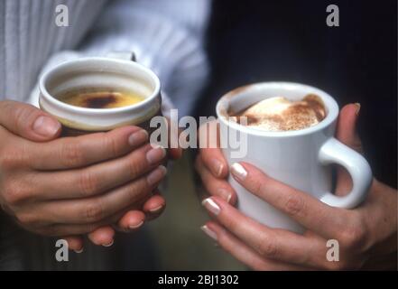 Heiße Getränke in den Händen - mit Milchschaum und Schokoladenpulver garniert - Stockfoto