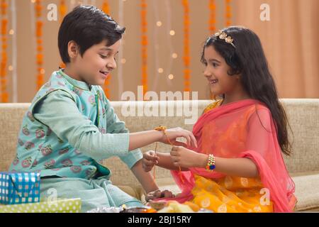 Kleines Mädchen, das Rakhi an ihren Bruder auf Rakshabandhan bindet Stockfoto