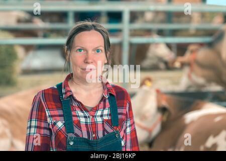 Frau Bauer über Kuh Dairy Farm. Portrait von Frau landwirtschaftlichen Arbeitnehmers tragen Plaid Shirt und bib Overalls im Kuhstall. Stockfoto