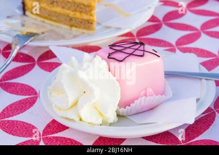 Vanillekuchen mit einem Twist und Schokoladenschwamm, bedeckt mit Erdbeerglasur, serviert mit Schlagsahne Stockfoto