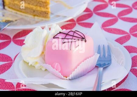 Vanillekuchen mit einem Twist und Schokoladenschwamm, bedeckt mit Erdbeerglasur, serviert mit Schlagsahne Stockfoto