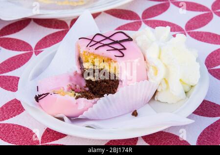 Vanillekuchen mit einem Twist und Schokoladenschwamm, bedeckt mit Erdbeerglasur, serviert mit Schlagsahne Stockfoto