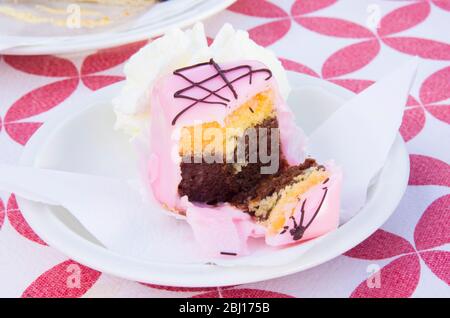 Vanillekuchen mit einem Twist und Schokoladenschwamm, bedeckt mit Erdbeerglasur, serviert mit Schlagsahne Stockfoto