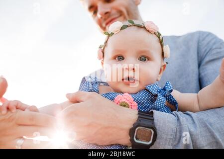 Der junge, schöne Vater hält die kleine Tochter in den Händen und lächelt an sonnigen Tagen. Frohe Familie. Vatertag Konzept. Papa erziehen ihre Tochter. Littl Stockfoto