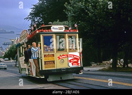 Passagiere an Bord einer aufsteigenden Cable Car-Linie, Powell-Hyde Line, San Francisco, Kalifornien, USA 1973. In diesem Jahr wurde das berühmte öffentliche Verkehrsnetz zum 100. Mal in den Mittelpunkt gestellt, und die Seilbahnen waren mit Schildern, Aschen und amerikanischen Flaggen geschmückt. Stockfoto