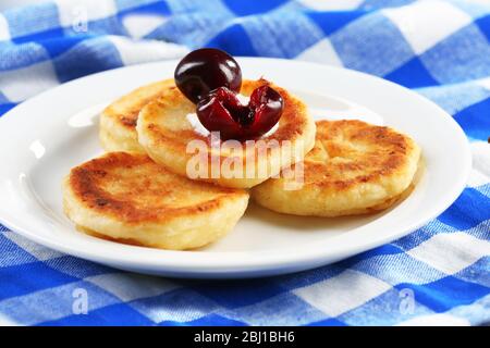 Quark-Fritten mit Kirsche und Sahne auf dem Teller auf karierter Serviette, Nahaufnahme Stockfoto