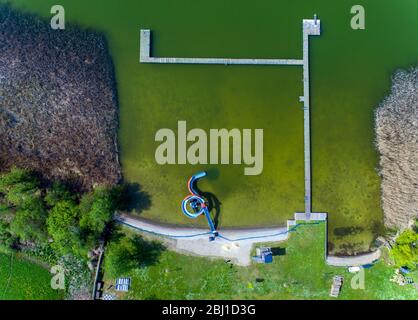 28. April 2020, Mecklenburg-Vorpommern, Bützow: Die leere Wasserrutsche steht am Ufer des Großen Rühner Sees im Freischwimmbad. (Luftaufnahme mit Drohne) aufgrund von Korona-Schutzmaßnahmen sind die Freibäder in Mecklenburg-Vorpommern geschlossen. Die Landesregierung will heute weitere Entscheidungen treffen, um Schritte aus der Blockierung der Korona zu Unternehmen. Für die bereits angekündigte Rückkehr von Zweitwohnheimbesitzern aus anderen Staaten nach MV und von Dauercampern zu den Plätzen ab dem 1. Mai sollen die notwendigen Regelungen verabschiedet werden. Foto: Jens Büttner/dpa-Zentralbild/dpa Stockfoto