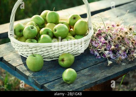 Grüne Äpfel mit Blumenstrauß auf Holztisch, Nahaufnahme Stockfoto