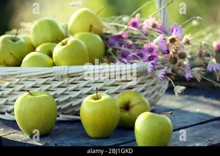 Grüne Äpfel mit Blumenstrauß auf Holztisch, Nahaufnahme Stockfoto