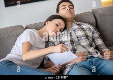 Dunkelhaarige Frau, die Papier hält und ihren Kopf auf der männlichen Schulter ruht Stockfoto