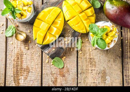 Sommerfrühstück mehrschichtiges Dessert mit Mango und Müsli. Mango Parfaits in portionierten Gläsern, rustikaler Holzhintergrund Kopierraum Stockfoto