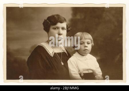 Anfang 1900 Foto von Jungen im Alter von etwa 3 Jahren mit bob Frisur, sitzt mit seiner Mutter, beide sehen ernst, Großbritannien um 1925 Stockfoto