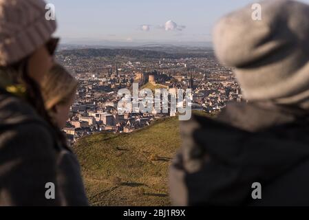 Eine Gruppe von Freunden auf dem Hügel Arthurs Seat mit Blick auf die Stadt Edinburgh und Edinburgh Castle, Schottland. Stockfoto