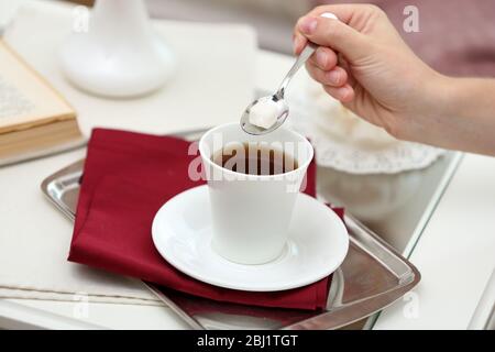 Weibliche Hand gießt Zucker in Tee auf dem Tisch Nahaufnahme Stockfoto