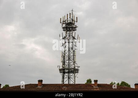 Antenne für Mobiltelefone hinter einem Hausdach. Mobilfunkturm an einem bewölkten Tag. Stockfoto