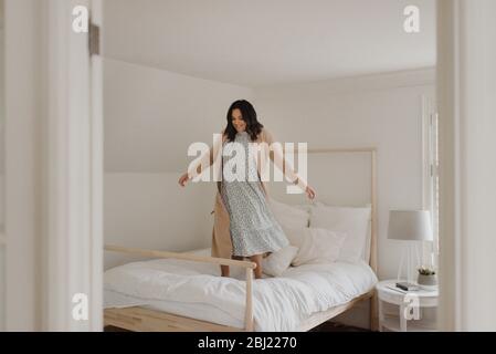 Frau mit langen dunklen Haaren, die vor Freude auf einem Bett springen. Stockfoto