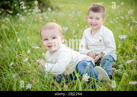 Porträt von zwei Jungen, die auf einer Wiese sitzen und vor der Kamera lächeln. Stockfoto
