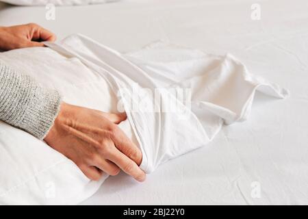 Nahaufnahme eines jungen kaukasischen Mannes, der ein Kissen in eine weiße Kissenhülle einführt, während er das Bett bildet Stockfoto