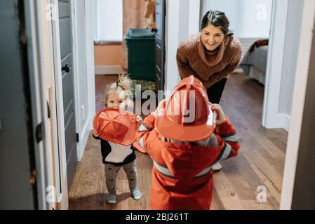 Eine Mutter lächelt ihr Kind an, das als Feuerwehrmann verkleidet ist. Stockfoto