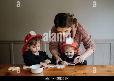 Eine Mutter hilft ihren beiden Kindern, Kekse mit Schokolade zu dekorieren. Stockfoto