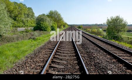 16.9 Ernte von parallelen Eisenbahnschienen in die Ferne mit üppigen grünen Bäumen umgeben, Büschen Straße unter blauem Himmel Stockfoto