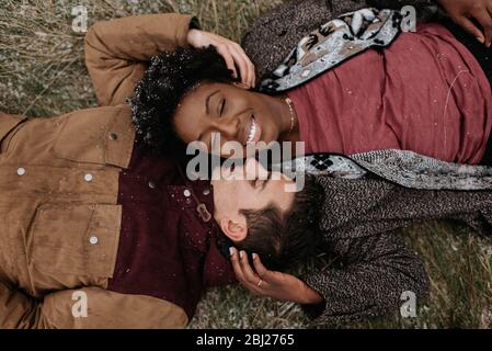 Blick von oben auf eine schwarze Frau und einen weißen Mann, der auf dem Boden liegt, mit einem Kopf zusammen und lächelnd. Stockfoto