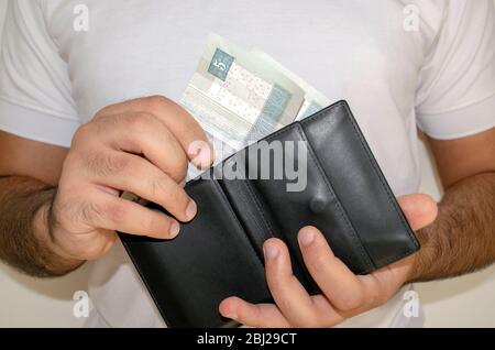 Ägyptens nationale Währung. Geldscheine. Mann in einem weißen T-Shirt legte ägyptische Pfund-Banknoten in die schwarze Brieftasche. Ein junger Mann hält in den Händen Geldbörse mit e Stockfoto