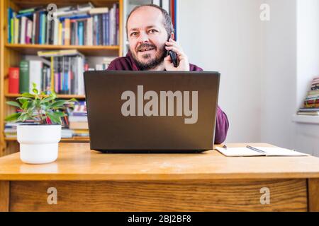 Mann, der vom Home Office aus arbeitet. Erwachsene bärtigen Mann konzentriert, online von zu Hause aus auf Computer-Laptop hinter Vintage-Schreibtisch arbeiten Stockfoto