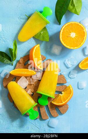 Hausgemachte Mops mit Orangensaft, Fruchteis, Lutscher auf blauem Stein- oder Schiefergrund. Draufsicht flach legen Hintergrund. Stockfoto