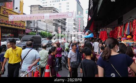 BANGKOK/THAILAND - FEBRUAR 15 2020: Belebte asiatische Innenstadt Straße mit Autos fahren entlang der engen Straße und Touristen kaufen traditionelle handgemachte Souvenirs in kleinen Geschäften am 15. Februar in Bangkok Stockfoto