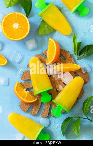 Hausgemachte Mops mit Orangensaft, Fruchteis, Lutscher auf blauem Stein- oder Schiefergrund. Draufsicht flach legen Hintergrund. Stockfoto