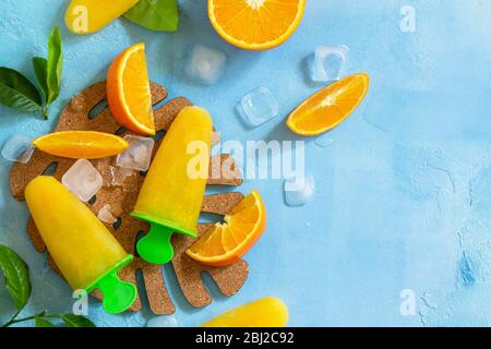 Hausgemachte Mops mit Orangensaft, Fruchteis, Lutscher auf blauem Stein- oder Schiefergrund. Draufsicht flach legen Hintergrund. Kopierbereich. Stockfoto