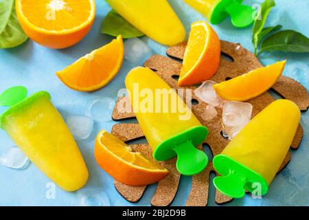Hausgemachte Mops mit Orangensaft, Fruchteis, Lutscher auf blauem Stein- oder Schiefergrund. Stockfoto