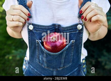 Rot reifen Apfel in die Tasche Blue Jeans Overalls. Landwirtschaft, Gartenbau, Ernte Konzept. Stockfoto