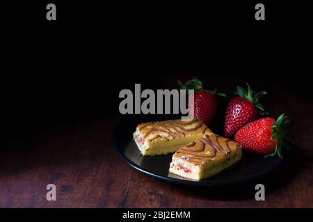 Biskuit-Kuchen mit Erdbeersirup-Füllung, mit Kakao-Belag dekoriert und mit frischen Erdbeeren auf einem schwarzen Teller serviert. Stockfoto