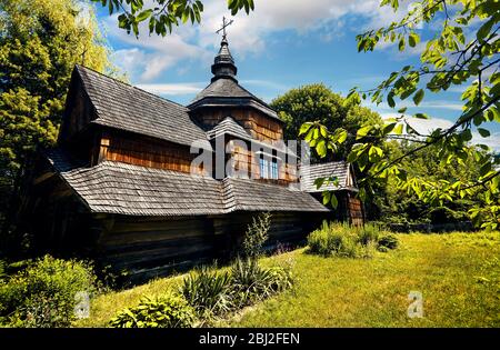 Alte Holzkirche, umgeben von üppiger Vegetation im traditionellen Dorf Osteuropa. Nationales Architekturmuseum in Pirogovo, Kiew, Ukraine Stockfoto