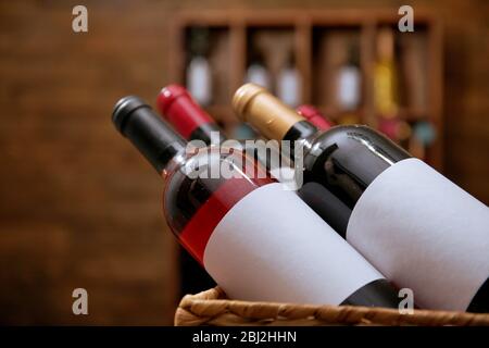 Geflaschter Korb mit beschrifteten Flaschen Wein auf unfokussiertem dunklen Hintergrund Stockfoto