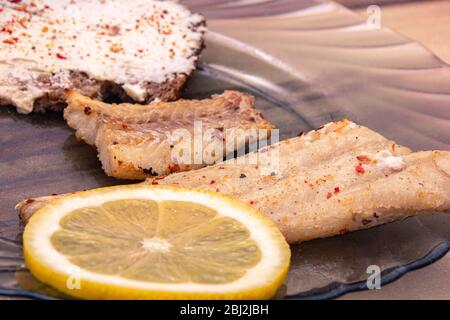 Nahaufnahme von gebratenem Seefisch mit Gewürzen, Zitrone und Brot auf dem Tisch Stockfoto