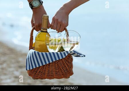 Junges Paar hält Picknickkorb mit einer Flasche Wein am Sandstrand Stockfoto