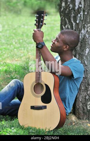 Schöner afroamerikanischer Mann mit Gitarre im Park sitzend Stockfoto