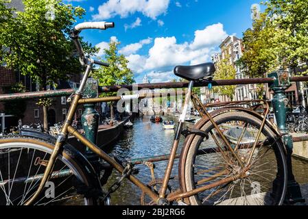 Altes rostig Vintage Fahrrad auf einer Brücke auf einem Kanal in Amsterdam, Niederlande geparkt Stockfoto