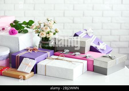 Dekorierte Geschenkboxen und Blumen auf dem Tisch vor weißem Backstein Wand Hintergrund Stockfoto