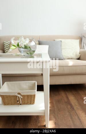 Pastellfarbenes Sofa mit wunderschönen Kissen und Vase mit Blumen auf dem Tisch davor im Zimmer Stockfoto