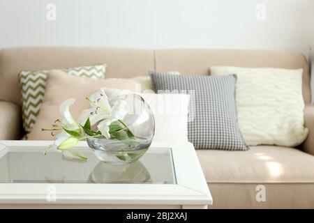 Pastellfarbenes Sofa mit wunderschönen Kissen und Vase mit Blumen auf dem Tisch davor im Zimmer Stockfoto