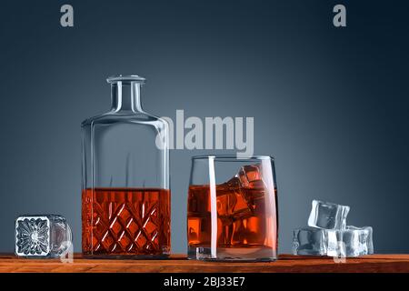 Ein Glas Whisky oder Cognac, ein Dekanter und Eiswürfel, ganz nah auf einem Holztisch. Blauer Hintergrund. Platz für Beschriftungen, Text und Logo. Layout für Adve Stockfoto