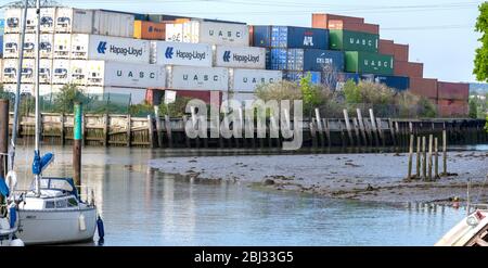 Blick auf Eling Creek mit hoch gestapelten Schiffscontainern auf Eling Wharf im Hintergrund, Totton, Hampshire, England, Großbritannien Stockfoto