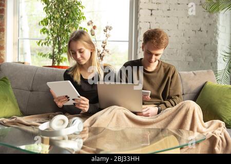 Attraktives junges Paar mit Geräten zusammen, Tablet, Laptop, Smartphone, Kopfhörer drahtlos. Kommunikation, Gadgets Konzept. Technologien, die Menschen in der Selbstisolierung verbinden. Lifestyle zu Hause. Stockfoto