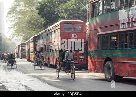 Dhaka / Bangladesch - 14. Januar 2019: Rikscha in der Allee mit großen roten Doppelstockbussen Stockfoto