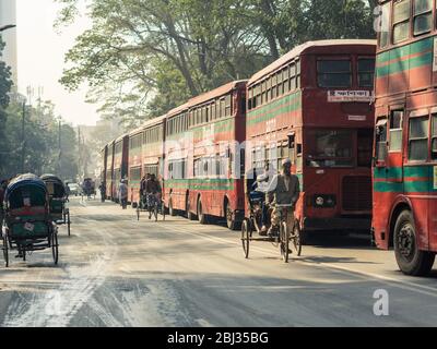 Dhaka / Bangladesch - 14. Januar 2019: Rikscha in der Allee mit großen roten Doppelstockbussen Stockfoto