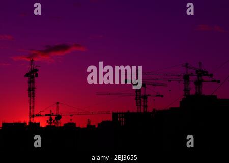 Bau Krane und Häuser schwarze Silhouette über Sonnenuntergang Himmel und Wolken Stockfoto